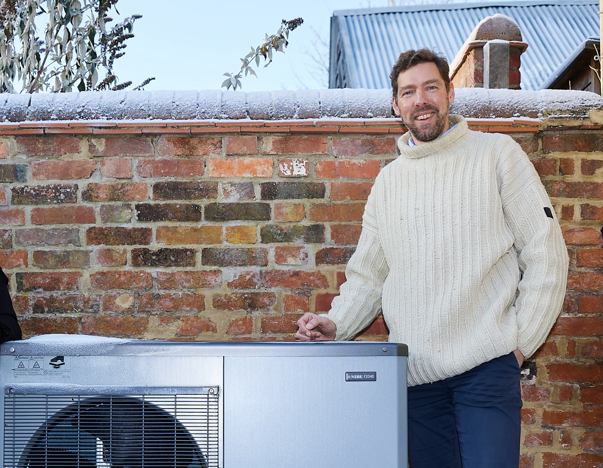 Dr Phil Grunewald, Research Director, Department of Engineering Science, University of Oxford, stands smiling next to a heat pump on a cold, snowy day